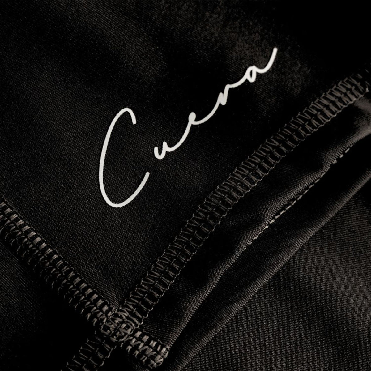 Detail van het witte Cuera-logo en de platte stiksels op de zwarte bikershort