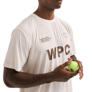Model in het gebroken witte Cuera WPC T-shirt houdt een padelbal in zijn hand