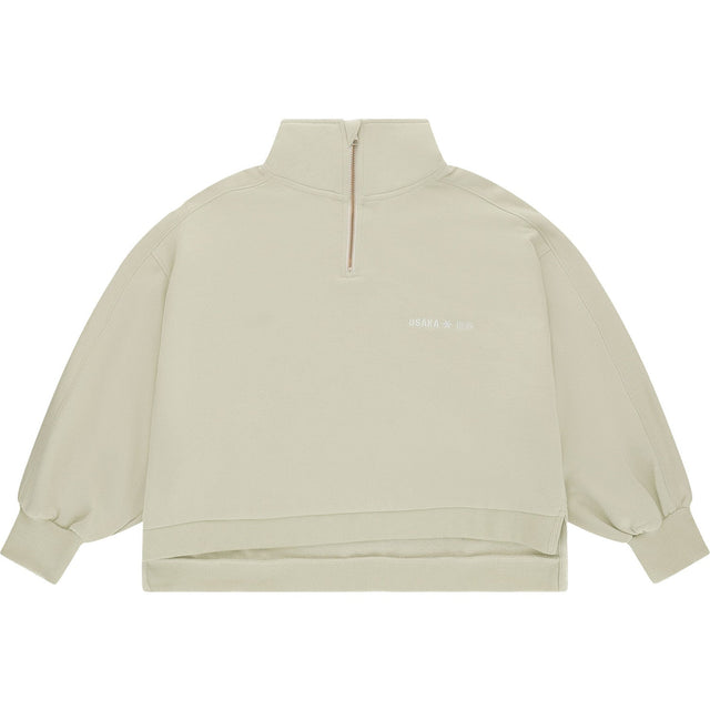 Vooraanzicht van de zandkleurige Osaka Cropped Half Zip Sweater met korte rits en logo