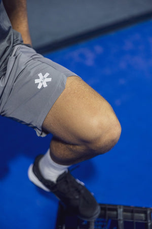 Speler zakt door de knieen in de grijze Osaka Men Training Short op de blauwe baan