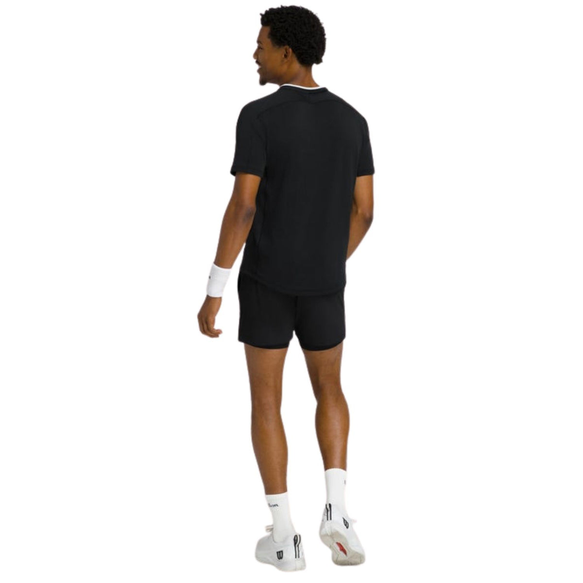 Model van achteren in het zwarte Wilson Serve Out T-shirt en padelschoenen