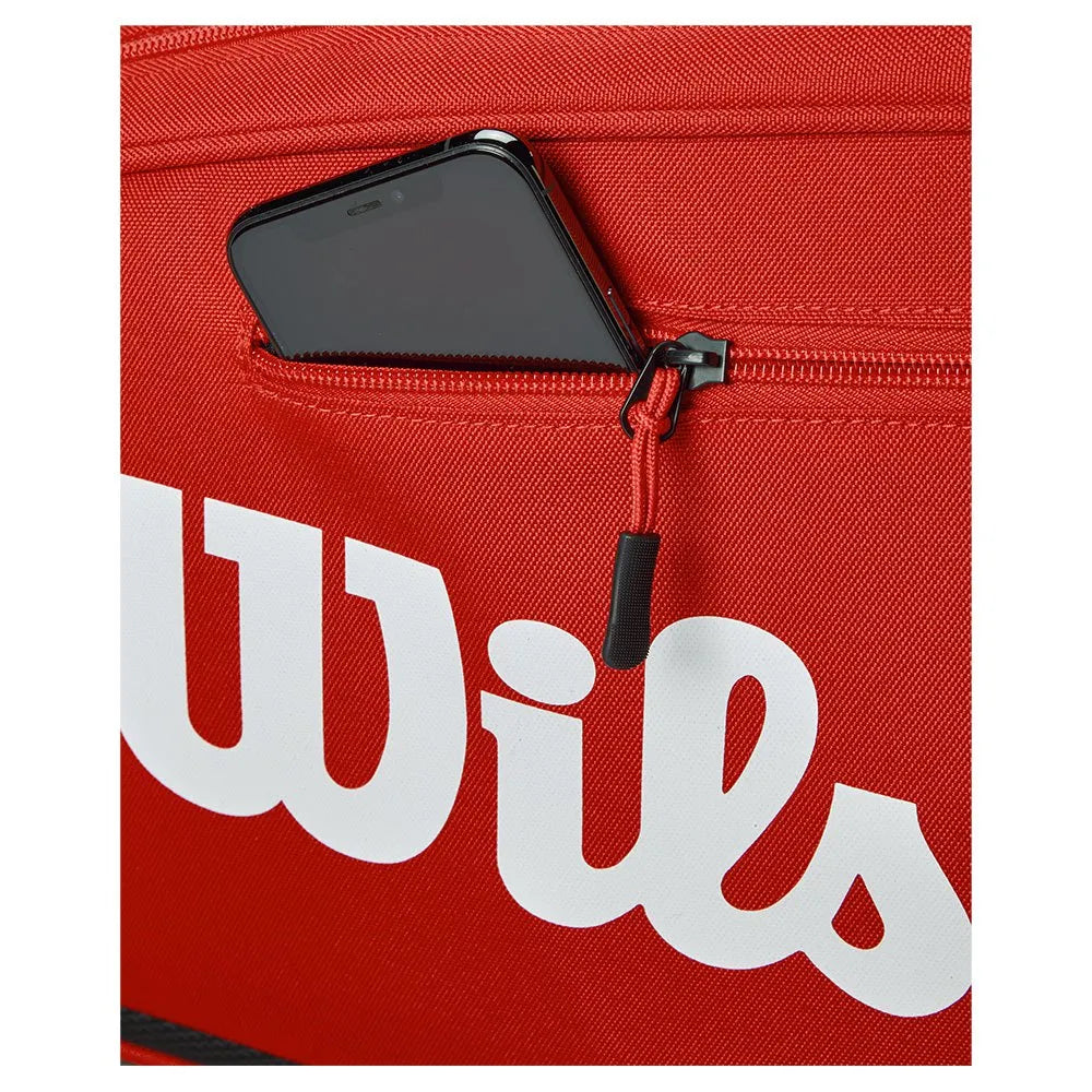 Detail van het witte Wilson logo en het ritsvak voor telefoon op de rode tas