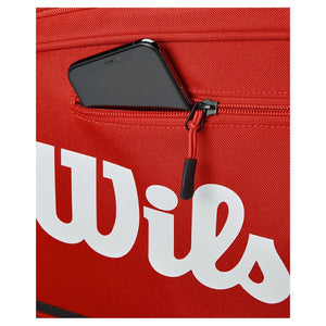 Detail van het witte Wilson logo en het ritsvak voor telefoon op de rode tas